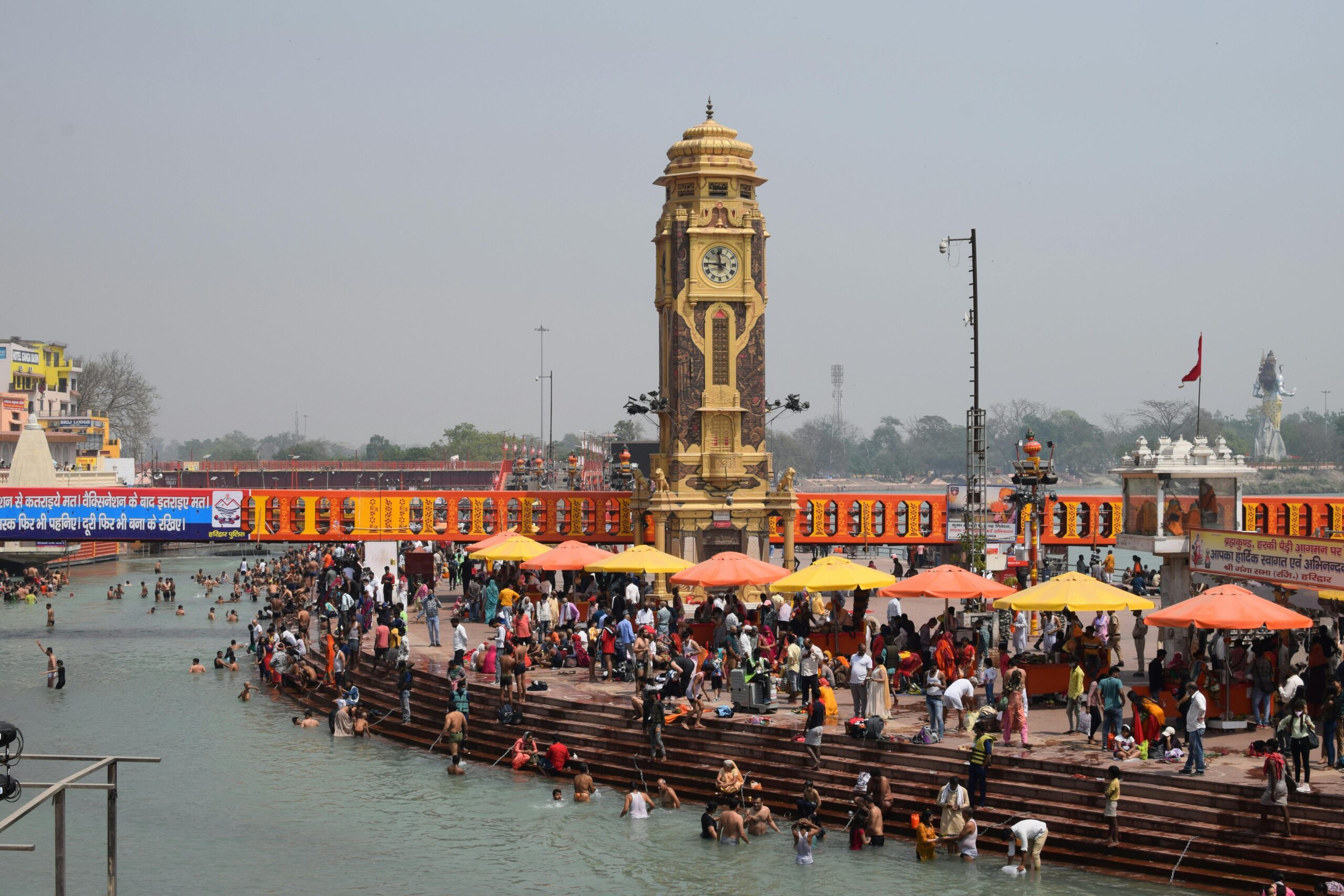 Vibrant scene of pilgrims bathing in Haridwar's Ganges with the iconic clock tower in view.